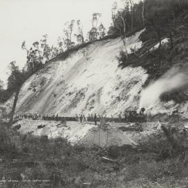 A group of workers at a quartz quarry at Mount Lyell, Tasmania.  A locomotive and wagons are visible.