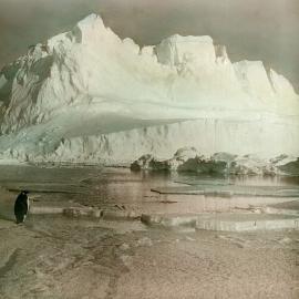 View of an iceberg with a penguin on floating ice in the foreground