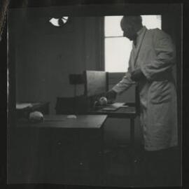 Man wearing laboratory coat with hooded rat, University of Melbourne Department of Psychology, 'Tin Hut' laboratory, Tin Alley