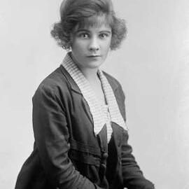 Studio portrait of a woman wearing a check blouse and dark jacket.