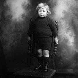 Studio portrait of a young Master Mitchell dressed in woollen clothes.