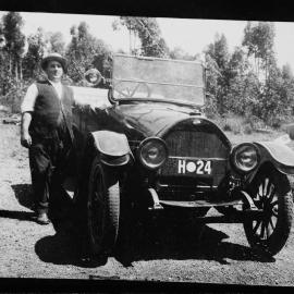 An unidentified man standing in bushland beside a car.