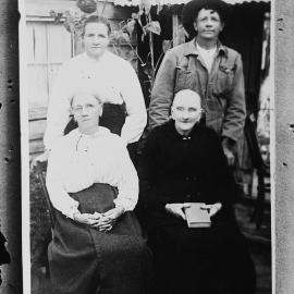 An unidentified group of four people outside a timber dwelling.