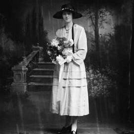 Studio portrait of Miss Scott wearing a black hat and holding flowers.