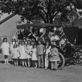 Young children standing in front of a car decorated with flags.