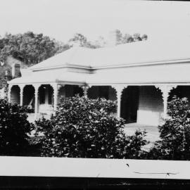 A large verandahed weatherboard house in front of a treed hillside.