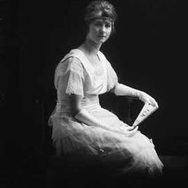 Studio portrait of Miss Dynon wearing long gloves and holding a fan.