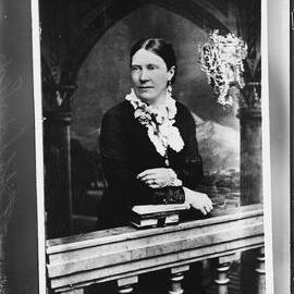 Portrait of a woman leaning on books on a balustrade.