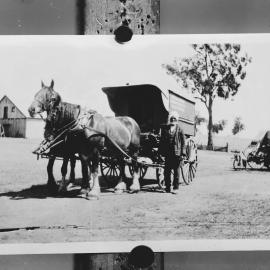 A man wearing a turban standing alongside a horsedrawn covered wagon.