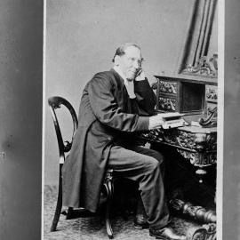 Portrait of an unidentified man seated at  a carved desk.