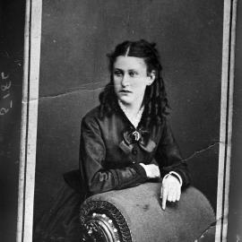 An unidentified young woman leaning on a chaise lounge.