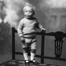 Studio portrait of an unidentified boy standing on a bench.