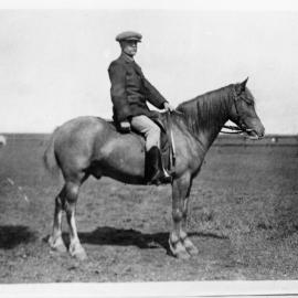 A moustached man wearing a cap and sitting astride a horse.
