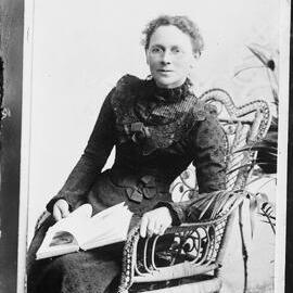 An unidentified  woman wearing spectacles and holding a book.