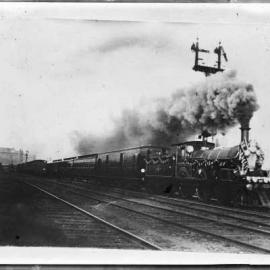 A locomotive with tender and carriages and under full steam, in an unidentified location.