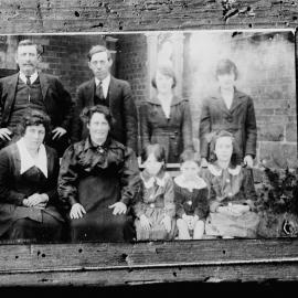 An unidentified group of nine people in front of a brick building.