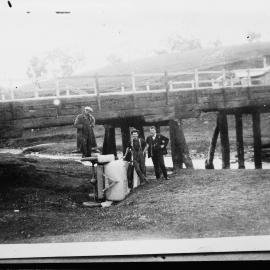 Men standing around a damaged car beneath a bridge.