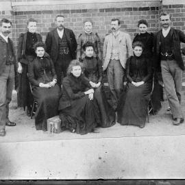 A posed group of unidentified people in front of a brick building.