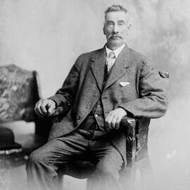 Studio portrait of an unidentified man in a carved chair.