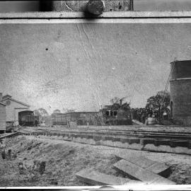 A railway line, railway buildings, locomotive and water tower.