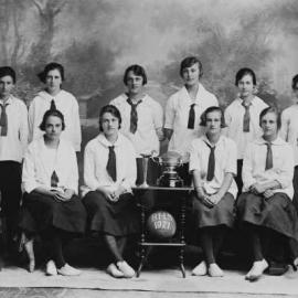 A posed team of young women with a ball and trophies.