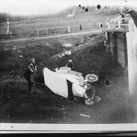 A damaged car beneath a bridge.
