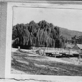 An unidentified rural scene including a cottage and a timber bridge.