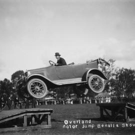 A car being driven across a gap between two timber ramps at the Benalla Show in 1921.