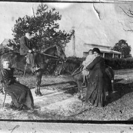 People and horses outside a timber cottage.