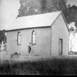 An unidentified woman standing outside a small public building.