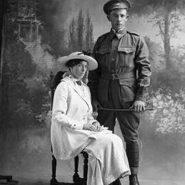 Studio portrait of a man in an Australian Army uniform and a woman wearing a large hat.   Family name Bevis.