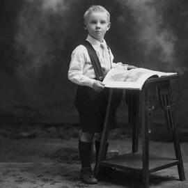Studio portrait of a boy holding a book.  Family name Greenwood.