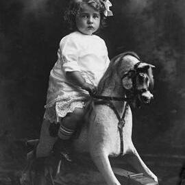 Studio portrait of a girl on a rocking horse.  Family name Rugg.