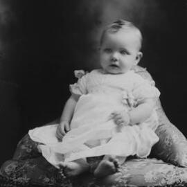 Studio portrait of a baby seated on a corner chair.   Family name Mortimor or Mortimer.