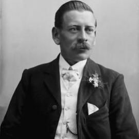 Studio portrait of a moustached man wearing a white waist-coat.