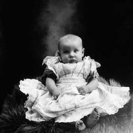 Studio portrait of a baby wearing a lace dress.   Family name Thurston.