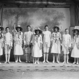 Young women and men dressed in costumes in front of a studio stage background.