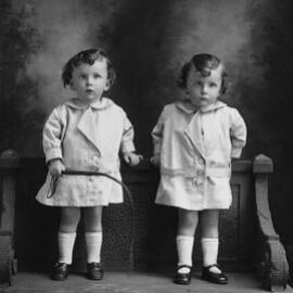 Studio portrait of two young girls standing on a bench.  Family name Keaney or Reaney.