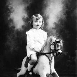 Portrait of a child seated on rocking horse.  Family name Carle.