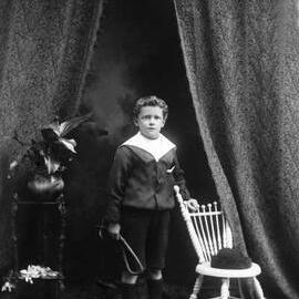 Studio portrait of a standing boy who holds a whip.  Family name Johnson.