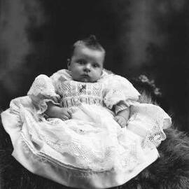 Studio portrait of a baby seated on a fur rug.   Family name Cook.