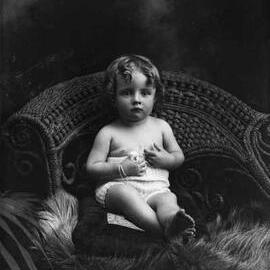 Studio portrait of a young child seated in a large wicker chair.  Family name Condon.
