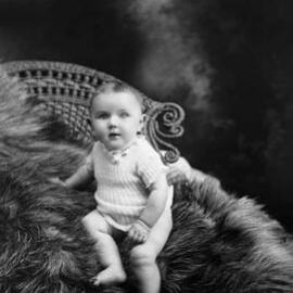 Studio portrait of a baby seated on a fur rug.  Family name Cutts.