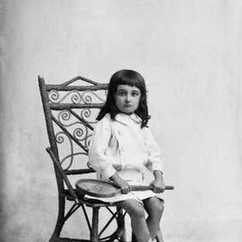 Studio portrait of a seated young girl holding a racquet.   Family name McKinnon.