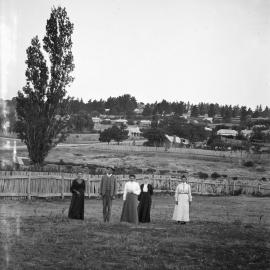 An unidentified group of people in a paddock with a town in the background..