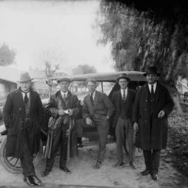 An unidentified group of well dressed men in front of a car.