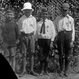 Group portrait of four unidentified boys in front of garden lattice.