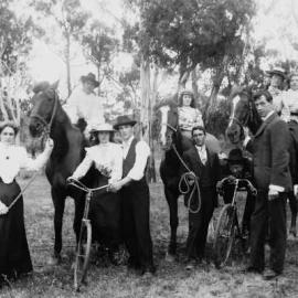 A group of young people with bicycles and horses, in a bushland setting, with a bridge visible.