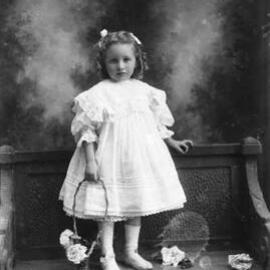 Studio portrait of a young girl wearing a lace trimmed dress.  Family name Mills.