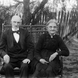 An unidentified elderly couple seated on a rustic bench.